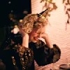 A person with curly hair and a party hat is laughing joyfully at a dinner table decorated festively. Soft lights and bokeh add a warm, celebratory ambiance to the scene.