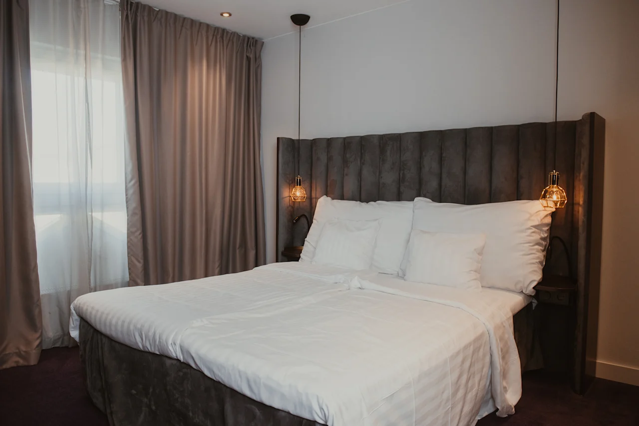 Ett mysigt hotellrum med en stor säng, vita lakan och varm belysning, redo för en bekväm vistelse.