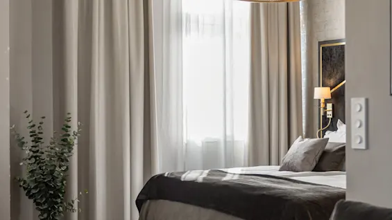 Et komfortabelt hotelværelse med en redt seng, bløde gardiner og en vase med friske blomster, der indbyder til afslapning.