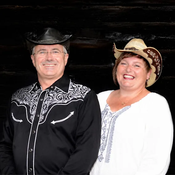 Smilende countryduo Steinar Engelbrektson og Sissel Sundby i cowboyhatter og westernskjorter foran en mørk trebakgrunn.