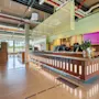 A modern and spacious hotel lobby with a long reception counter, bar stools, and large windows overlooking an outdoor area.