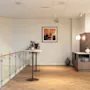 A bright, modern hotel common area with wooden floors, a glass railing, and a refreshment station.
