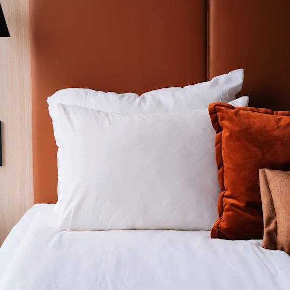 Ett mysigt hotellrum på Quality Hotel Arlanda XPO med en säng, vita och orange kuddar, och en fjärrkontroll på ett sängbord.