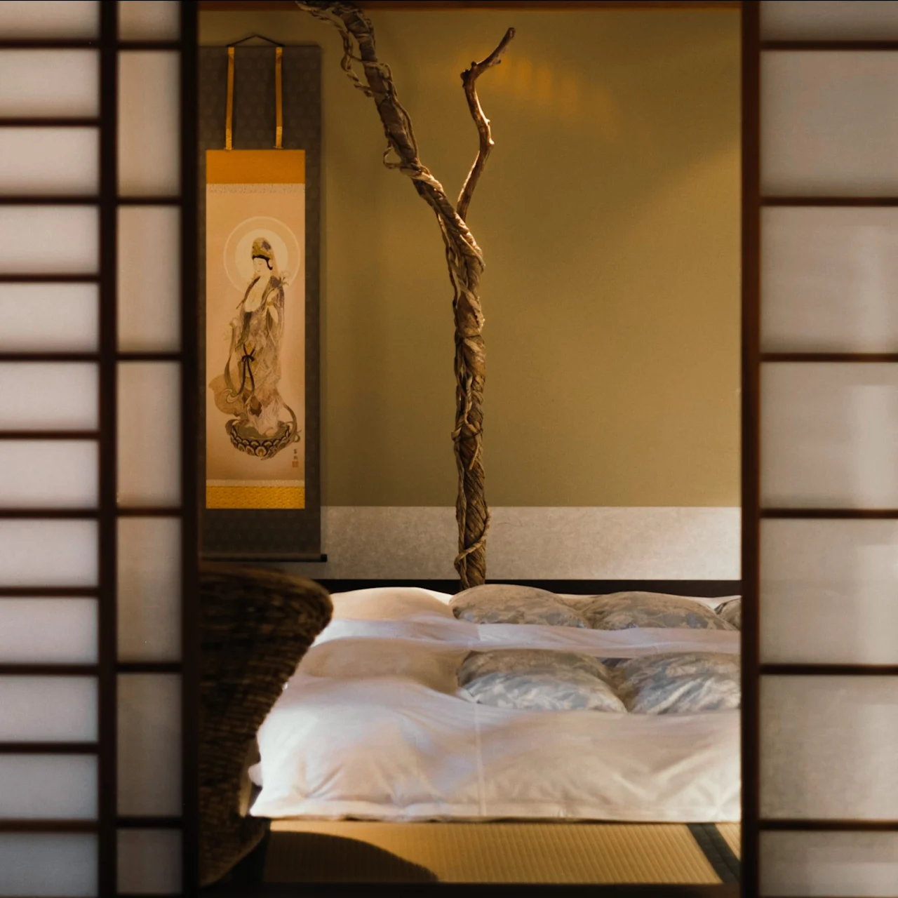 En lugn sovrumsscen genom en shoji-skärm, med en mjuk säng, en dekorativ gren och en traditionell rullmålning.