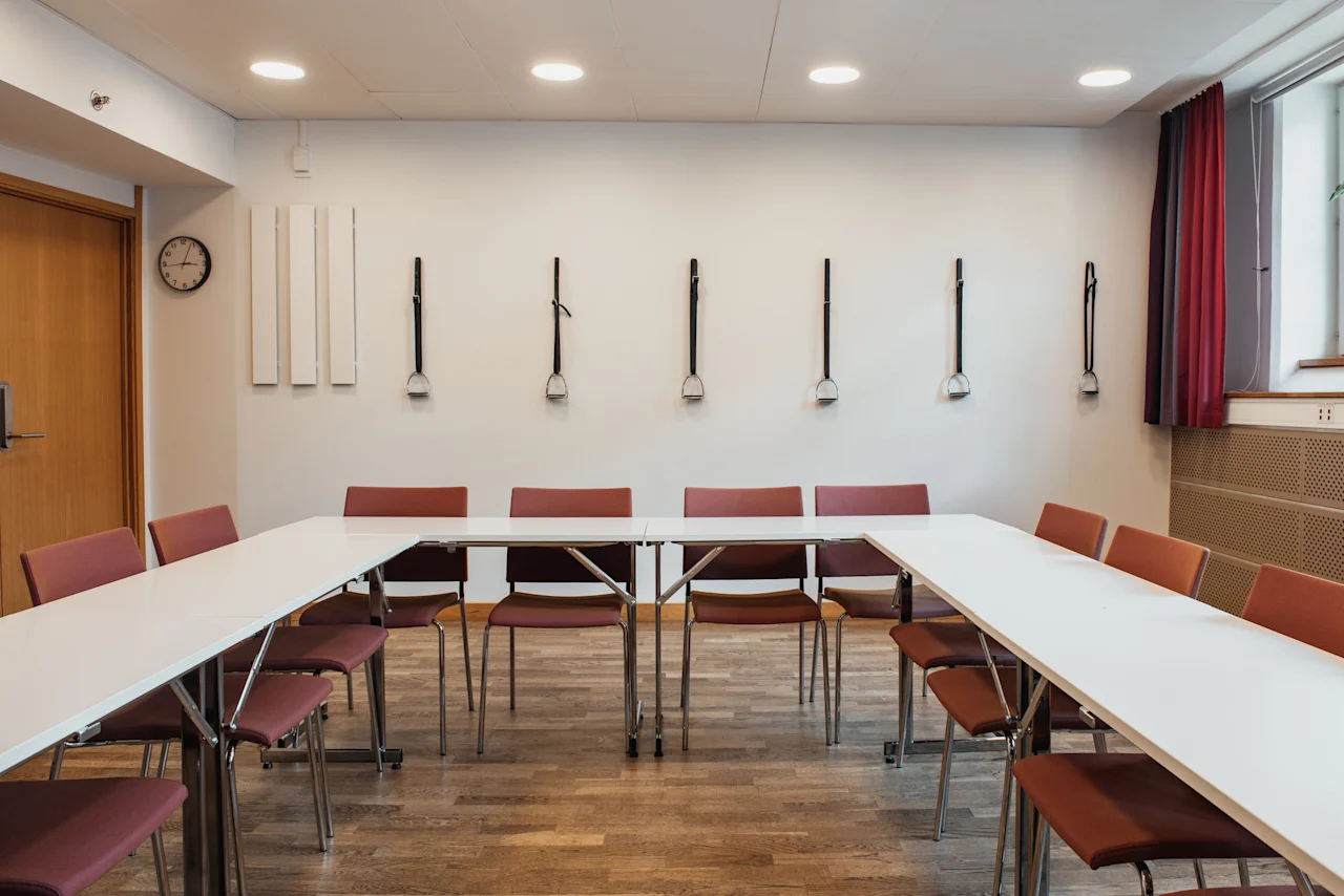 A conference room at Home Hotel Uppsala with a U-shaped table and chairs, decorated with stirrups on the wall.