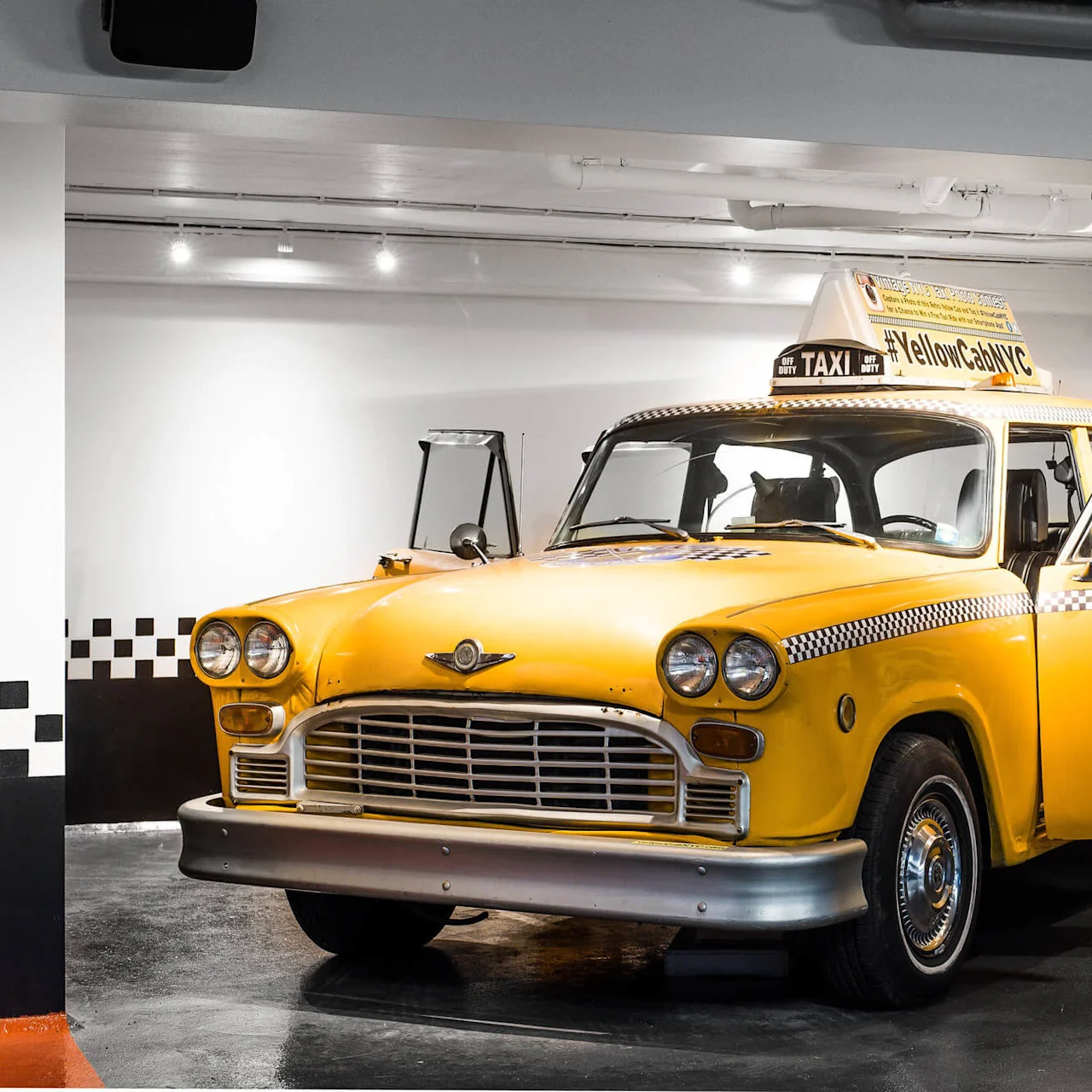 En klassisk gul taxibil med schackrutiga detaljer, parkerad inomhus.