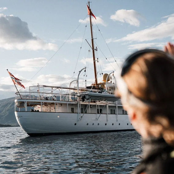 En person ser på det hvite kongeskipet som seiler på fjorden med et norsk flagg heist.