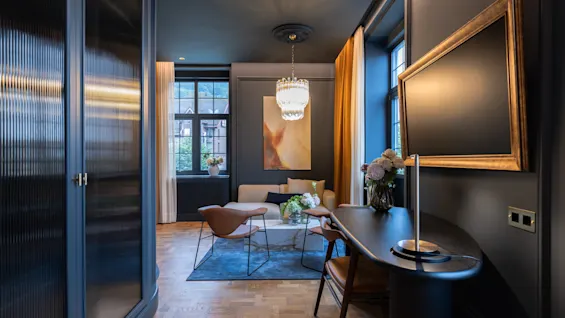 Elegant and dark hotel room featuring a stylish seating area, a desk, and a beautiful chandelier.
