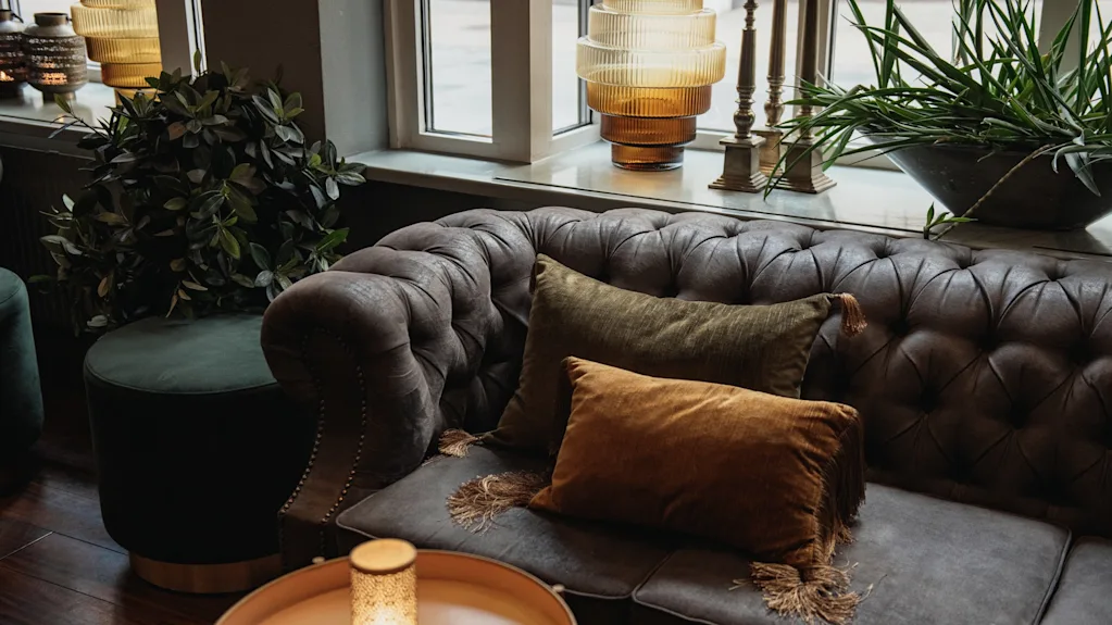 En bekväm och inbjudande loungeavdelning med en tuftad soffa med plyschkuddar, stämningsbelysning och frodig grönska.