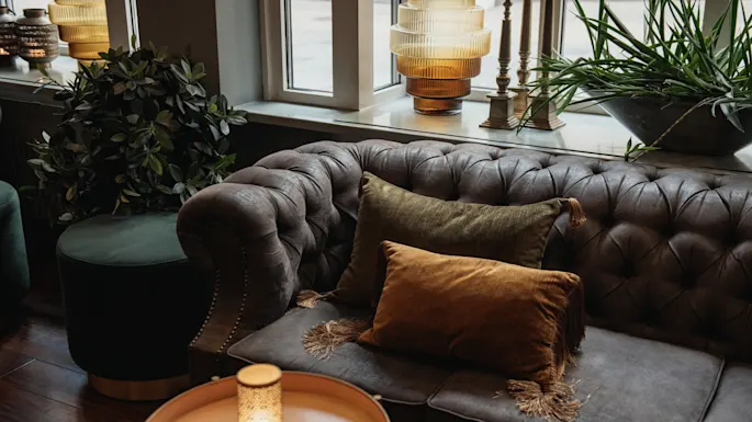 Et komfortabelt og innbydende salongområde med en tuftet sofa med myke puter, stemningsbelysning og frodig grønt.