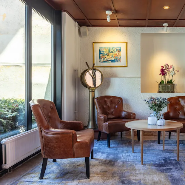 A cozy seating area with four leather armchairs around a wooden coffee table, indoors with natural lighting and decorative flowers.