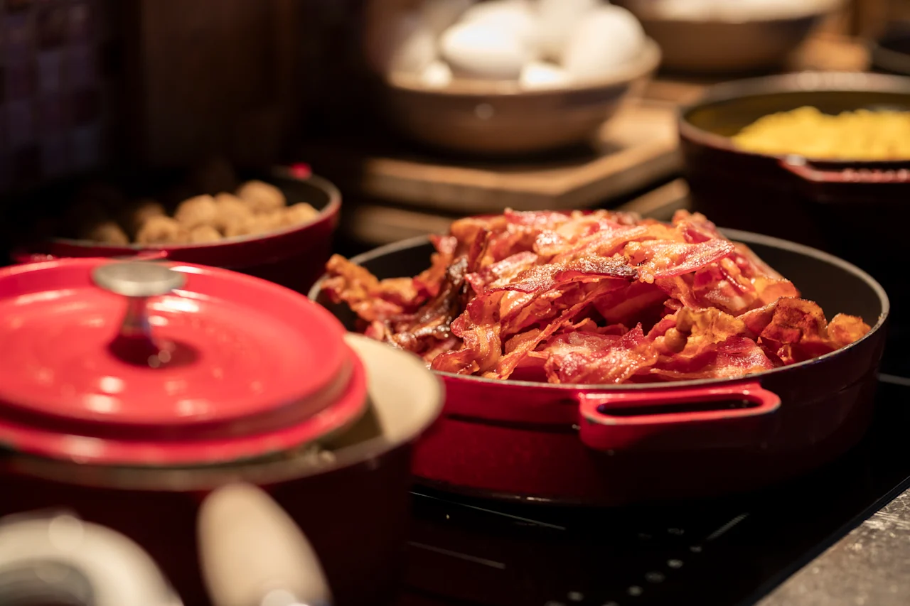 Eloisa aamiaisbuffet, jossa on suuri punainen pata täynnä rapeaa pekonia ja muita herkullisia aamiaisruokia.