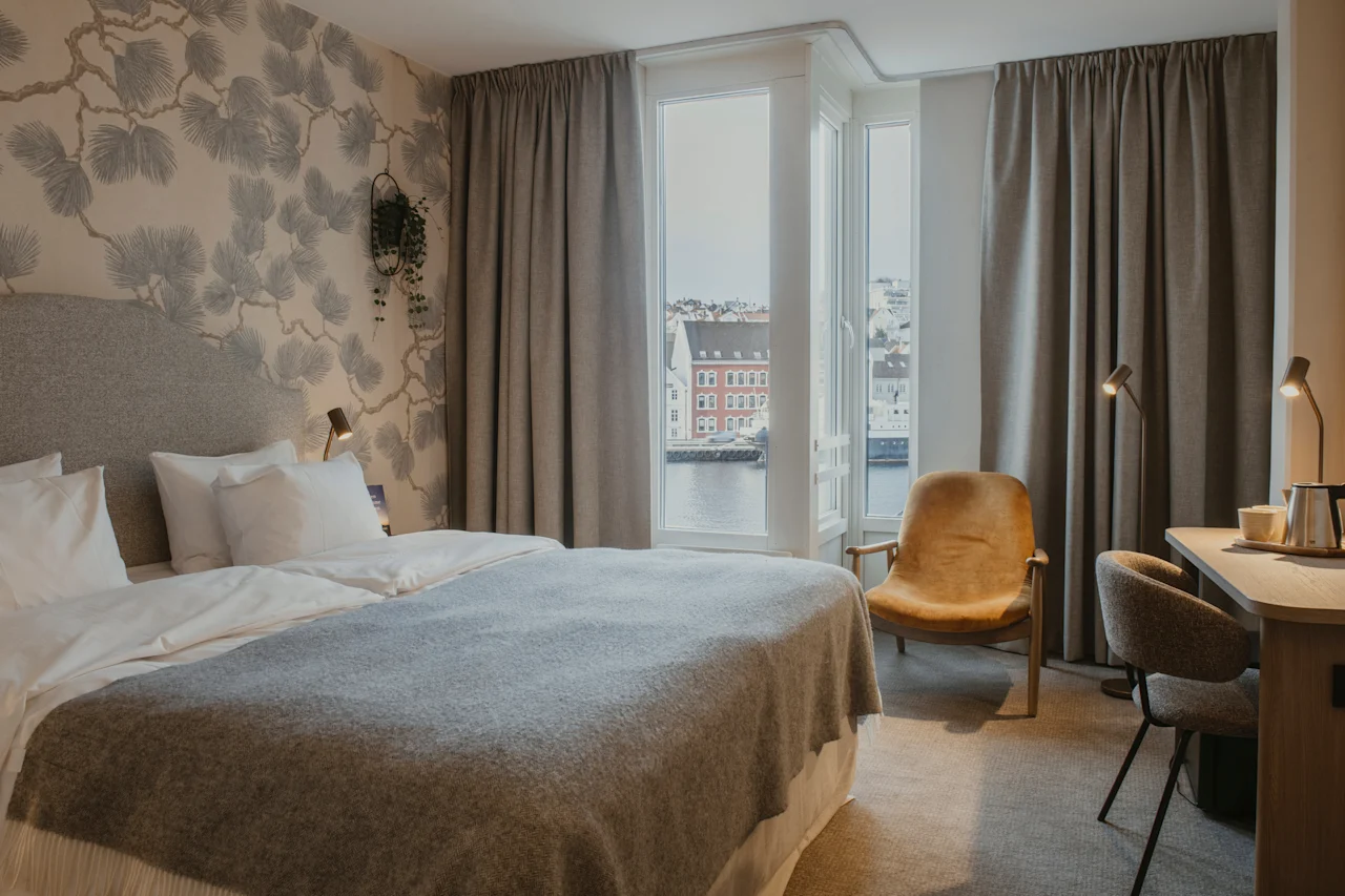 Et hyggeligt hotelværelse med en stor seng, et skrivebord og et vindue med udsigt over en by og vand.