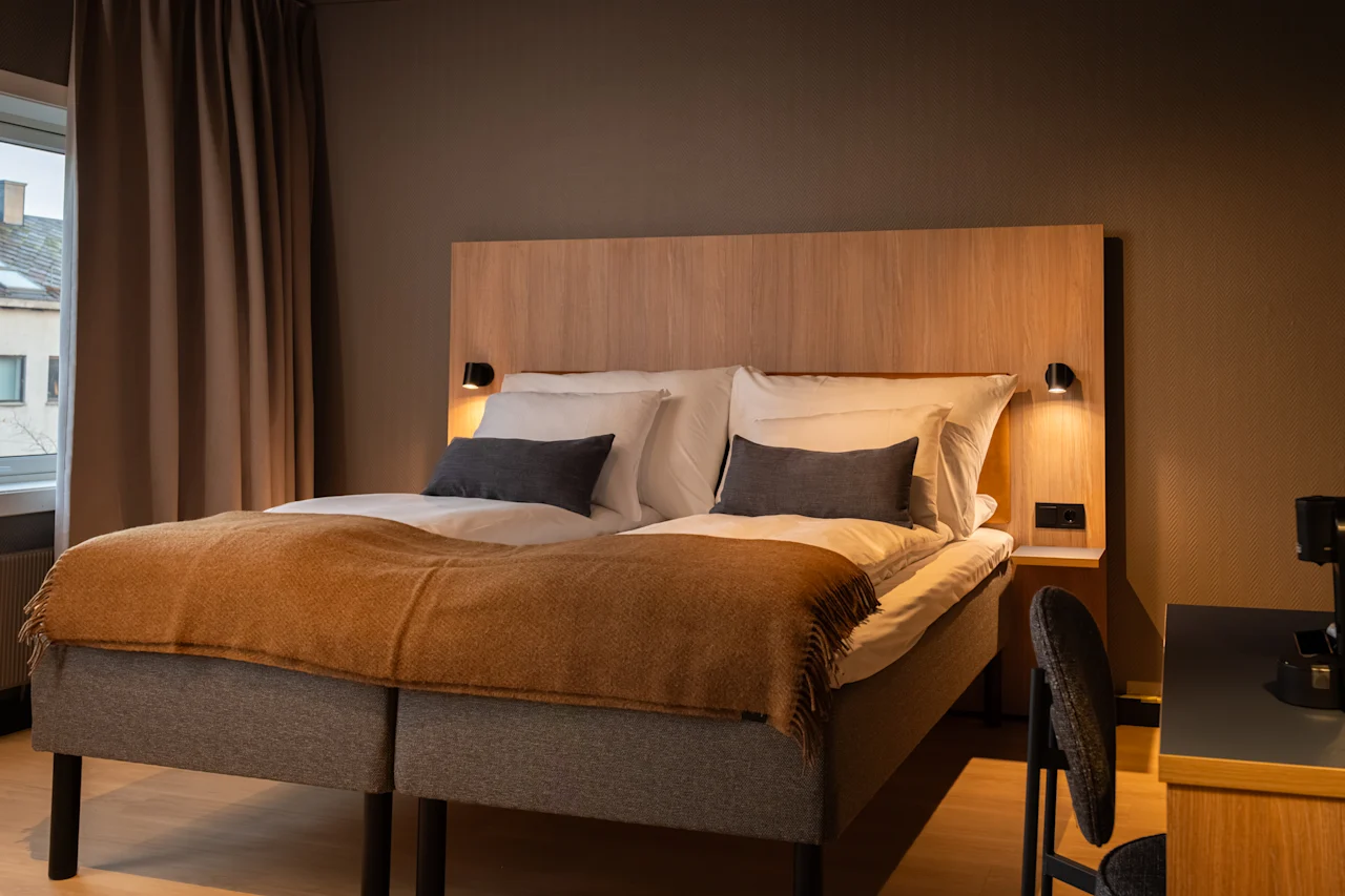 A cozy hotel room with two beds, warm lighting, and a window with curtains. An inviting space for rest and relaxation.