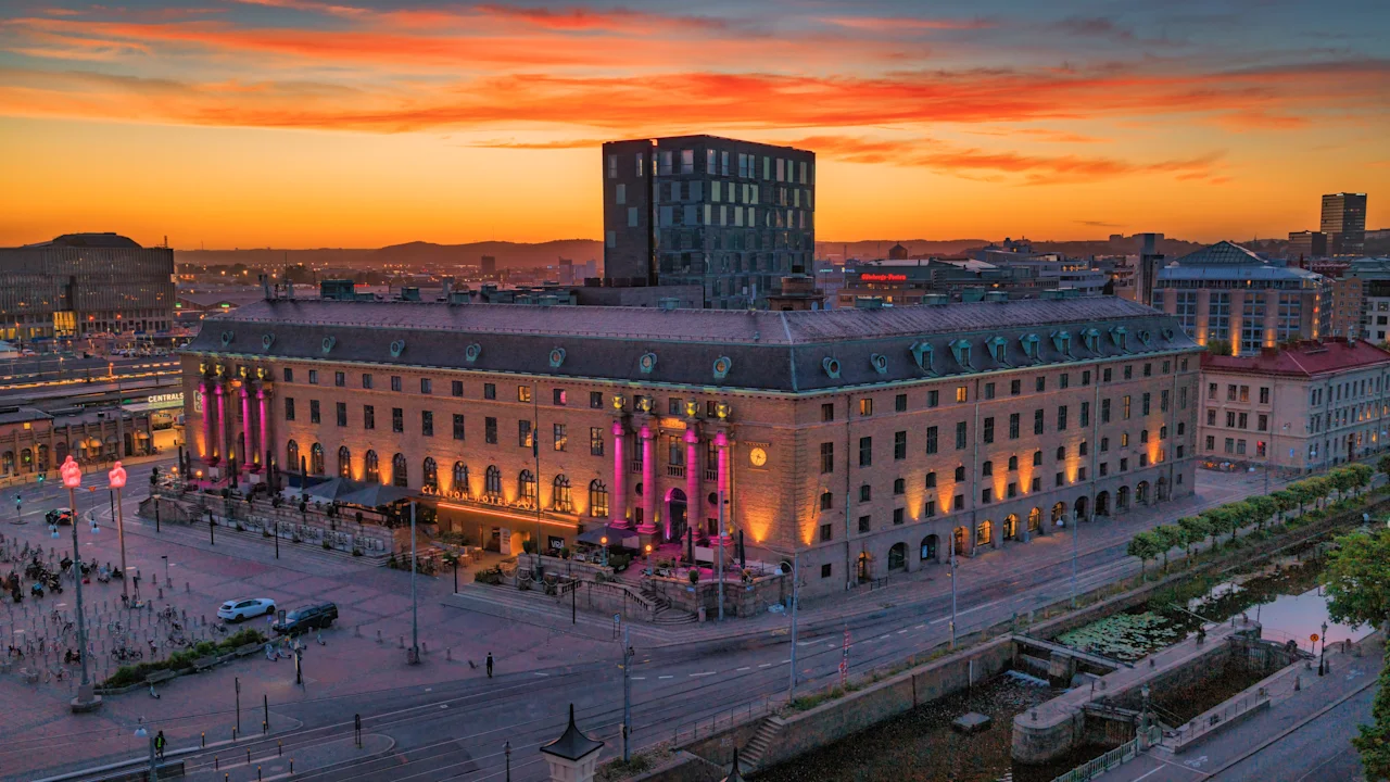 Ett stort hotell i klassisk stil upplyst i rosa och gult under en färgstark solnedgång i staden.