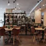A cozy restaurant interior with wooden tables, leather chairs, and shelves filled with bottles and books, illuminated by warm hanging lights.