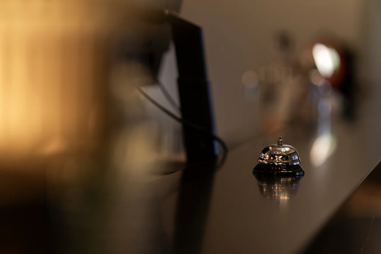 A shiny service bell on a dark, reflective counter at Home Hotel Grand Bodø, awaiting a guest's ring for assistance.