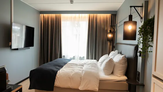 Et moderne hotellrom med en komfortabel seng, veggmontert TV og stilig belysning.