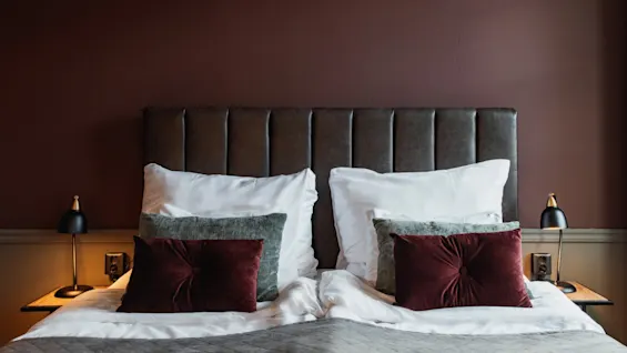 En mysig sovrumsscen med en prydligt bäddad säng med mjuka kuddar och varm belysning, inbjudande till avkoppling.