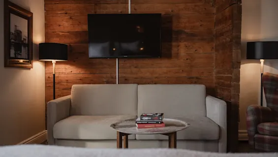 Et hyggeligt opholdsområde med en lys sofa, et sofabord med bøgerne GW og Management, og et TV på en rustik trævæg.