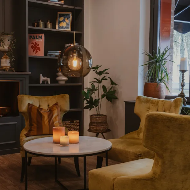 Cozy hotel lounge with armchairs, fireplace, and decorative items. A book titled PALM is visible. Home Hotel Kung Oscar.