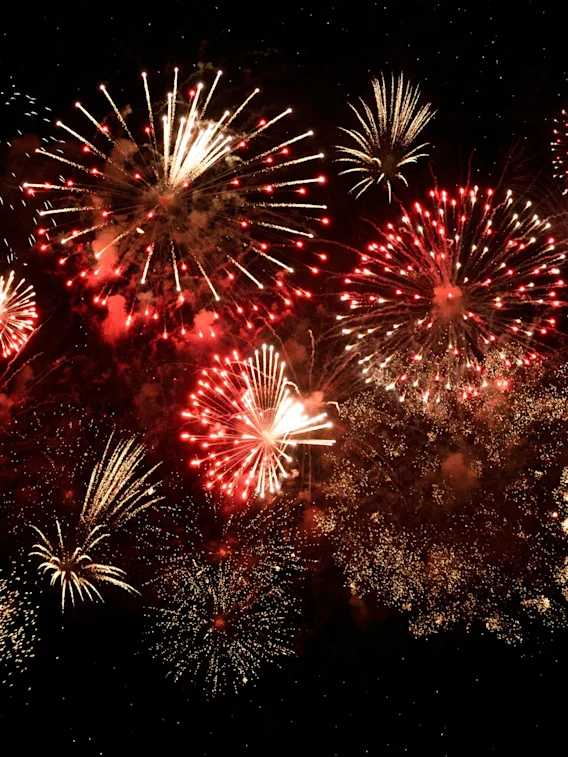 A vibrant fireworks display illuminates the dark night sky with bursts of red and golden light.