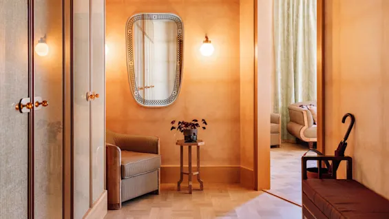 Et varmtonet rom med teksturerte vegger, speil, garderobe, lenestol og paraplystativ, som utstråler en koselig og vintage atmosfære.