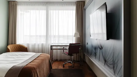 Ett modernt hotellrum med bekväm säng, skrivbordsplats och stort fönster med skira gardiner. Ett ljust och inbjudande utrymme.