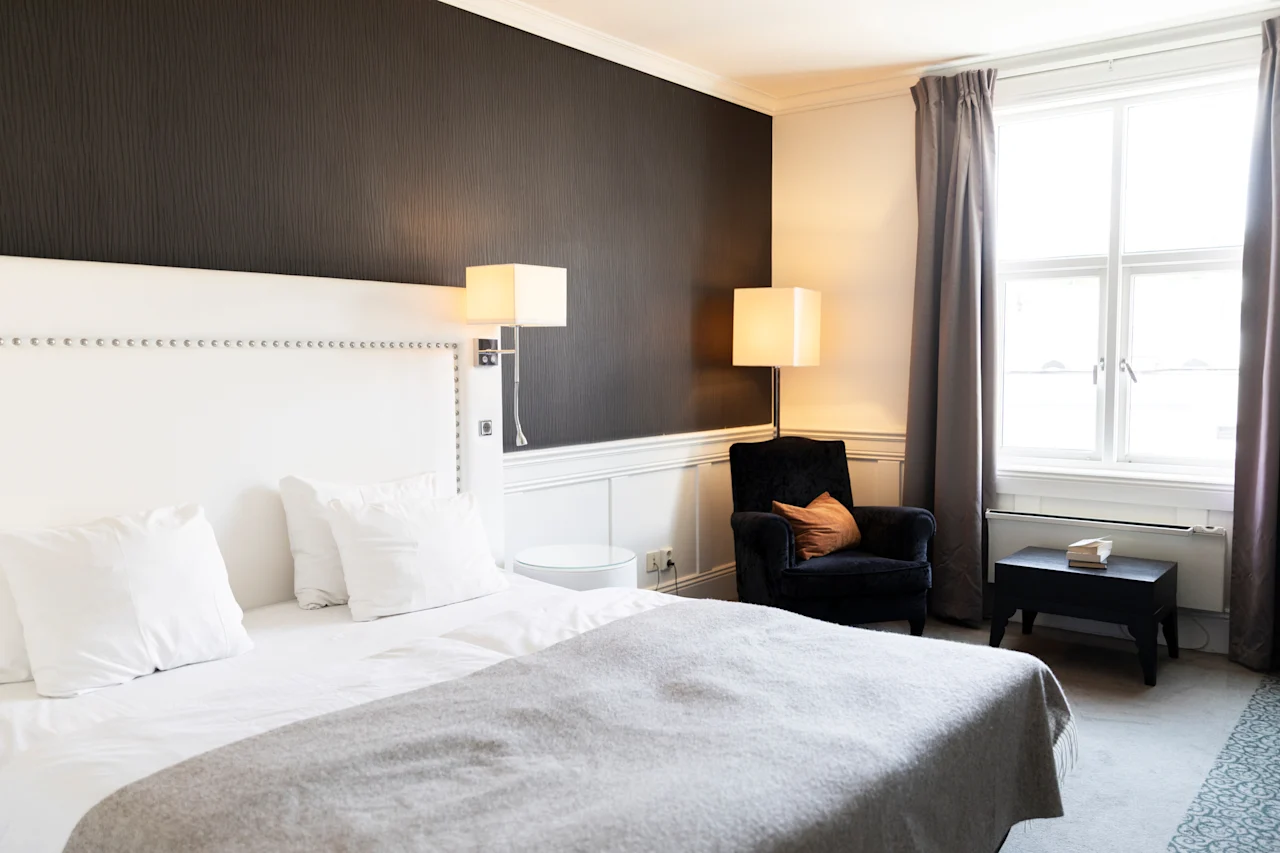 Et indbydende hotelværelse med en plys seng, en komfortabel lænestol og blød belysning, der skaber en rolig atmosfære.