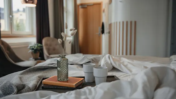 A cozy hotel room at Home Hotel Uppsala with a bed, a tray with books, dried flowers, and two cups, ready for a relaxing moment.