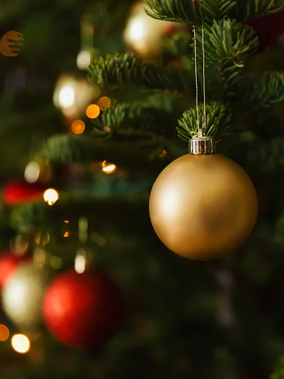 Et nærbilde av et juletre pyntet med gylne og røde julekuler, med varme, uskarpe lys i bakgrunnen.