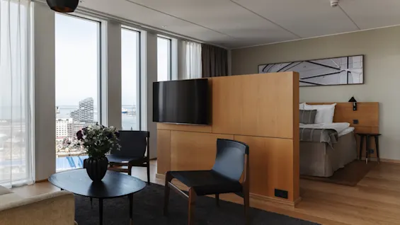 Et moderne hotellrom med stue, soverom og store vinduer som tilbyr en naturskjønn utsikt over byen.