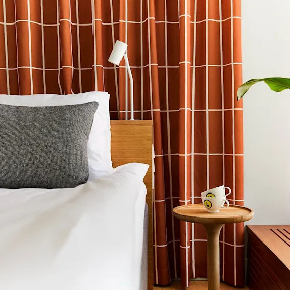 A warm and inviting bedroom with a neatly made bed, patterned curtains, a plant, and a small table with two cups.