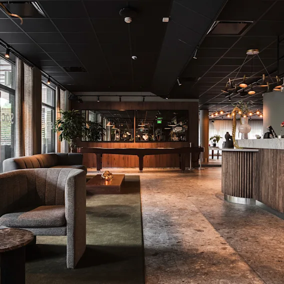 En stilfull hotellounge med en välfylld bar, bekväma sittplatser och ett biljardbord, badad i naturligt ljus.