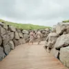 Två personer i badrockar går hand i hand på en trästig mellan stenmurar och gräsbevuxna kullar.