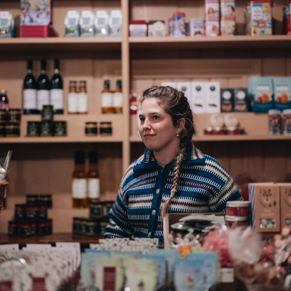 A person working behind the counter in a cozy grocery store filled with shelves of products