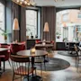 Et stilfullt restaurantinteriør med ulike sitteplasser, levende lys på bordene og store vinduer mot en bygata. HOTEL TEMPEL.