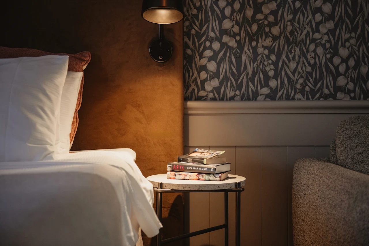 En hyggelig læsekrog med en seng, et sidebord med bøger inklusive ASYL og VILSE, og blød belysning.