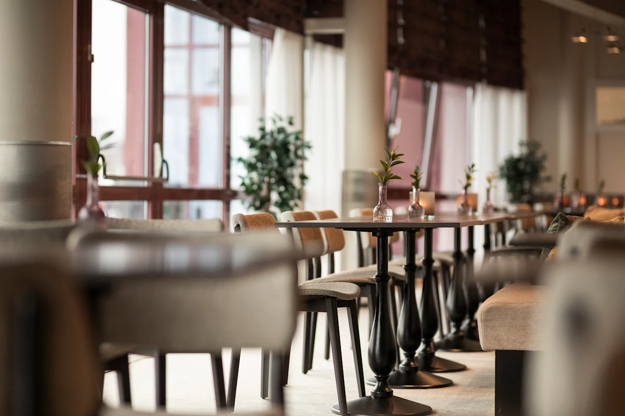 A cozy restaurant or cafe interior with rows of tables and chairs, bathed in natural light from large windows, creating a welcoming atmosphere.