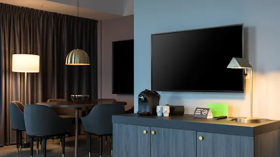 TV på en vegg, med kaffemaskin og lampe på et skap i nærheten. Bak, et bord med stoler under hengende belysning. Et skilt på skapet sier, "THANK YOU FOR NOT SMOKING".