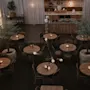Runda träbord med tända ljus arrangerade i en mysig, svagt upplyst restaurang med krukträd och mjuka gardiner. Området runt omkring inkluderar en disk och hyllor med dekorativa föremål.