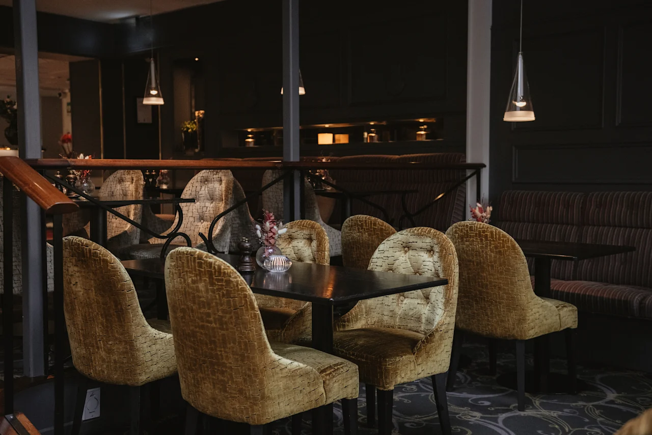 A cozy dining area at Home Hotel Kung Oscar with golden upholstered chairs and dark tables, set for a relaxing meal.