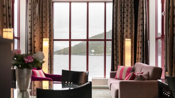 Viihtyisä huone, jossa on suuri ikkuna ja josta avautuu luonnonkaunis näkymä järvelle ja vuorille.