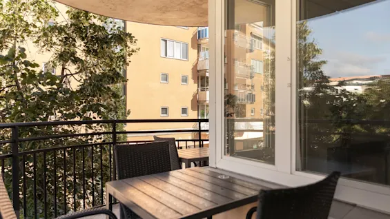 Balkong på Home Hotel Tapto med utemöbler, med utsikt över en byggnad och träd en solig dag.