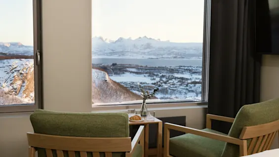 Et hyggeligt værelse med to stole vendt mod et stort vindue, der tilbyder en fantastisk udsigt over snedækkede bjerge og en by ved vandet.