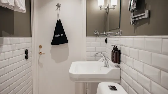 Home Hotel Baltzar - Standard Twin: A clean bathroom with a sink, toilet, mirror, and a hair dryer bag hanging on the door.
