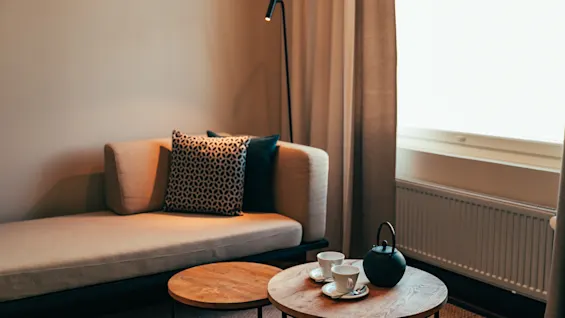 En mysig hörna med en schäslong, två bord, en tekanna och koppar, vilket antyder en avkopplande paus.
