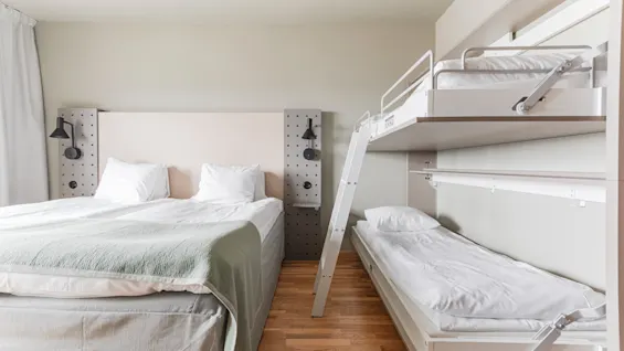 A hotel room with a double bed on the left and a bunk bed system on the right, featuring a top bunk and a pull-out bed.