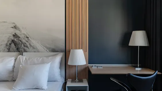 A modern hotel room at Clarion Hotel Sign with a bed, bedside lamp, and a desk area with a chair and lamp.