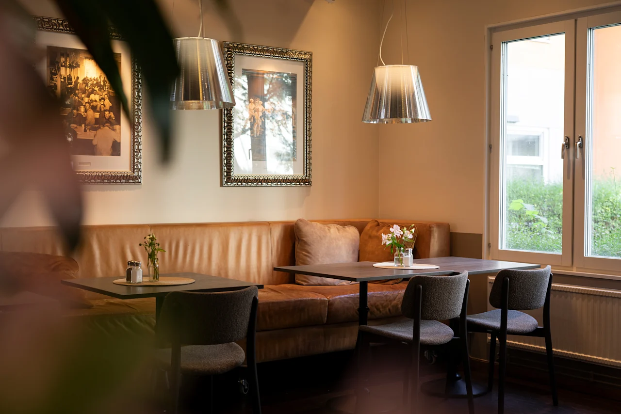 En varm och inbjudande kaféinteriör med bekväma sittplatser, bord dukade för gäster och naturligt ljus från ett fönster.